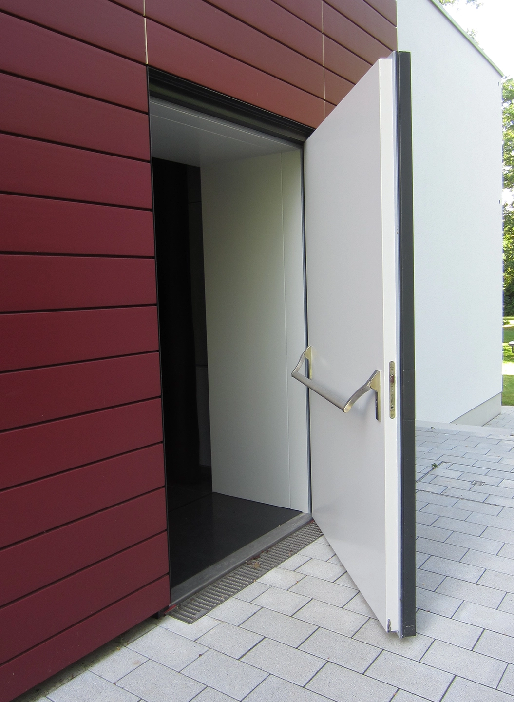 Weiße Schallschutztür mit Panikstange in roter Fassade, geöffnet