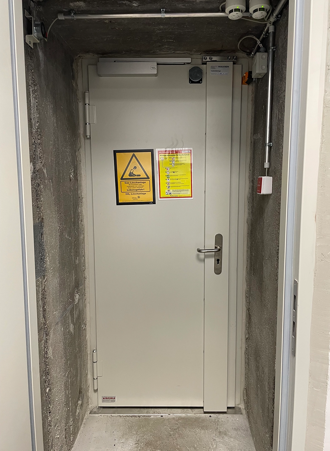 Weiße druckbeständige Tür von BUCHELE in einem Betonschacht mit Warnschildern
