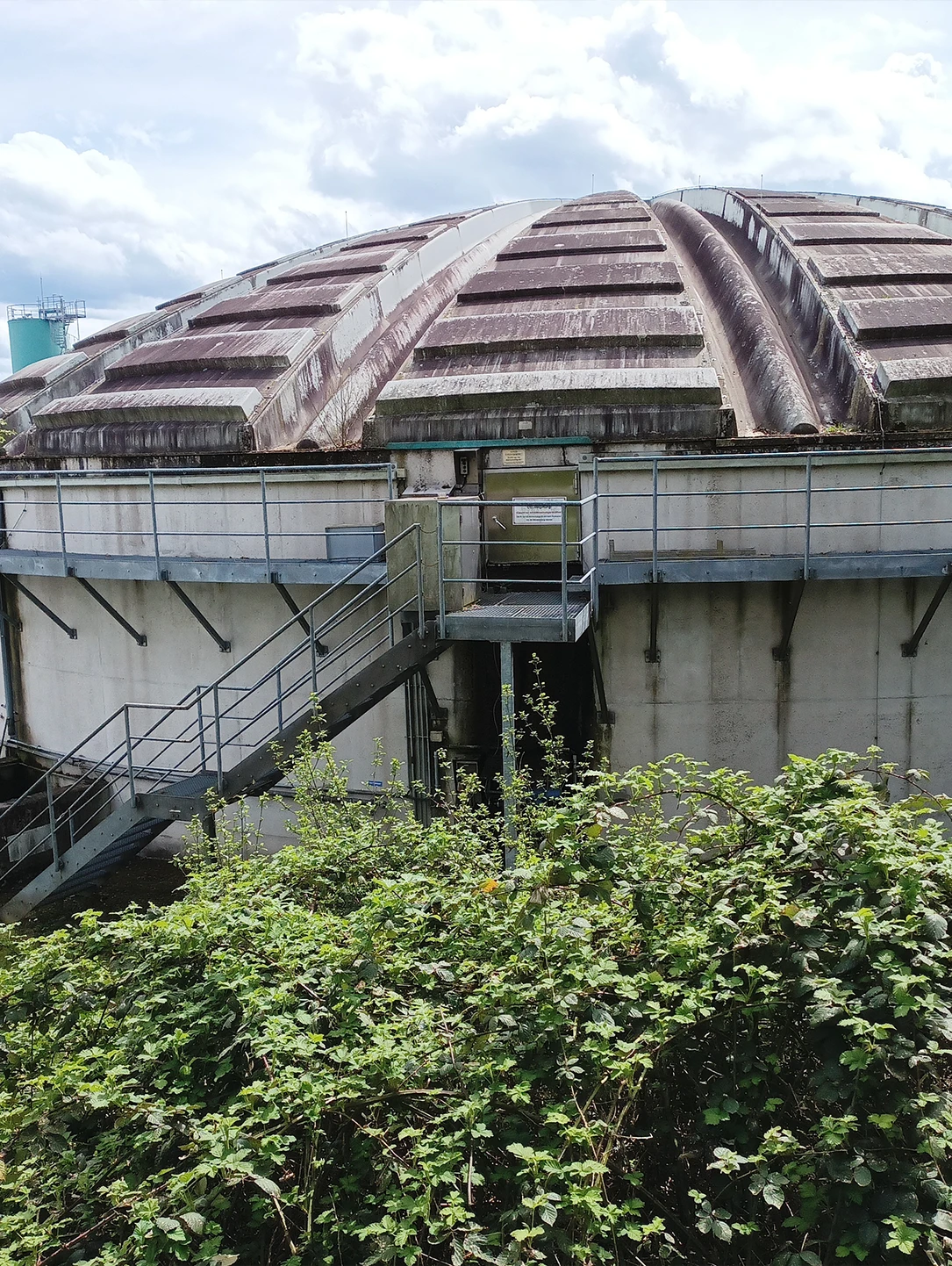 Kuppelgebäude einer Kraftwerksanlage mit Stahltreppe und Bewuchs