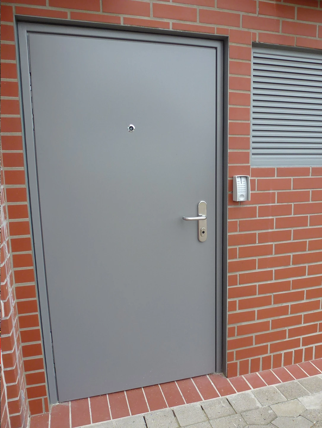 Graue Sicherheitstür von BUCHELE in einer Klinkerfassade neben einem Lüftungsgitter