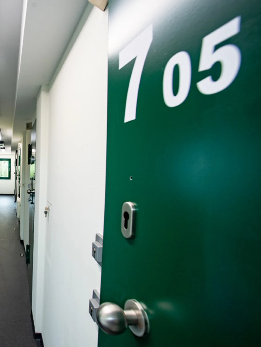 Grüne Hafttür mit Nummer 705 und Sicherheitsschlössern in einer Justizvollzugsanstalt