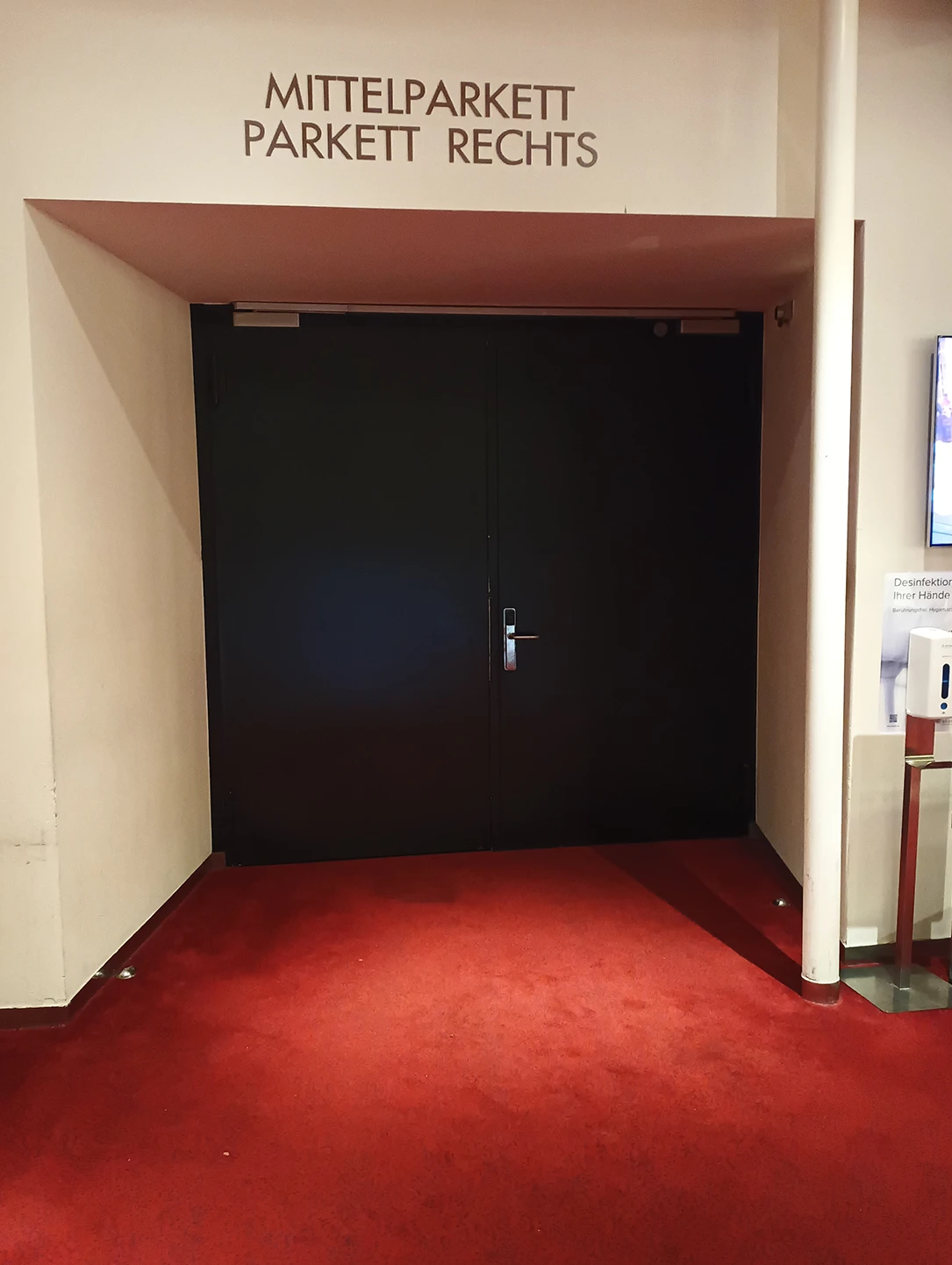 Schwarze Schallschutztür zum Mittelparkett eines Theatersaals mit rotem Teppich