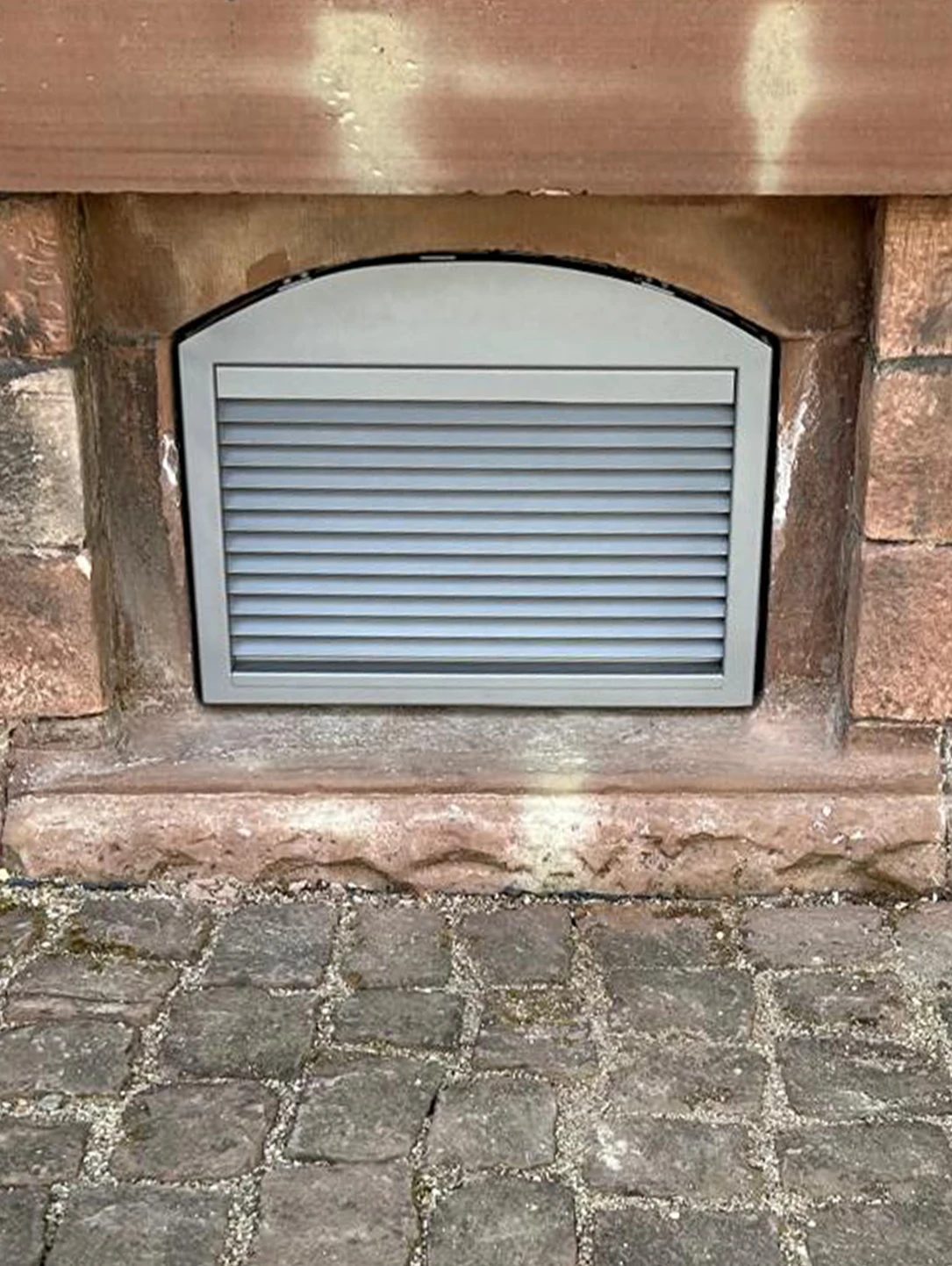 Graues Lüftungsgitter von BUCHELE in einem Sandstein-Fensterbogen