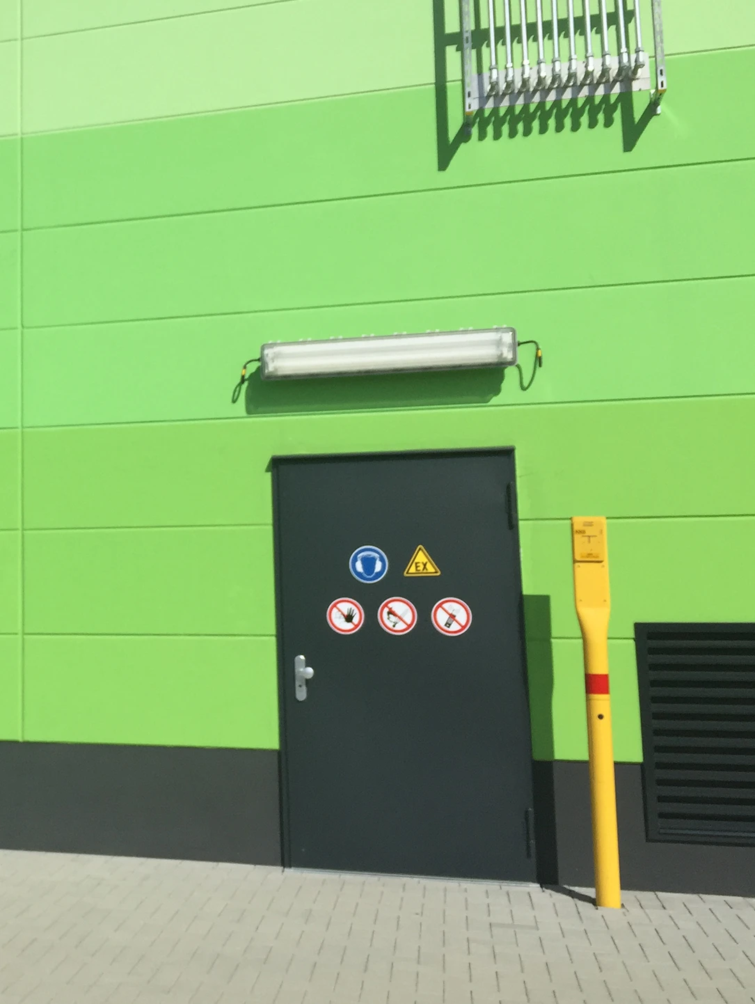 Dunkelgrüne Ex-Schutztür mit Warnschildern in einer grünen Fassade