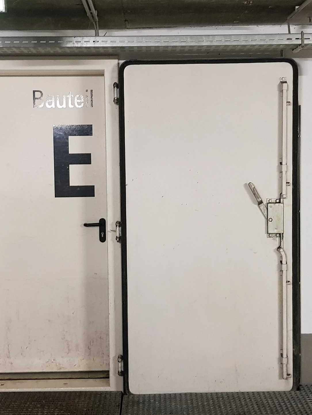 Weiße Hochwasserschutztür von BUCHELE mit Verriegelungshebeln, Beschriftung Bauteil E