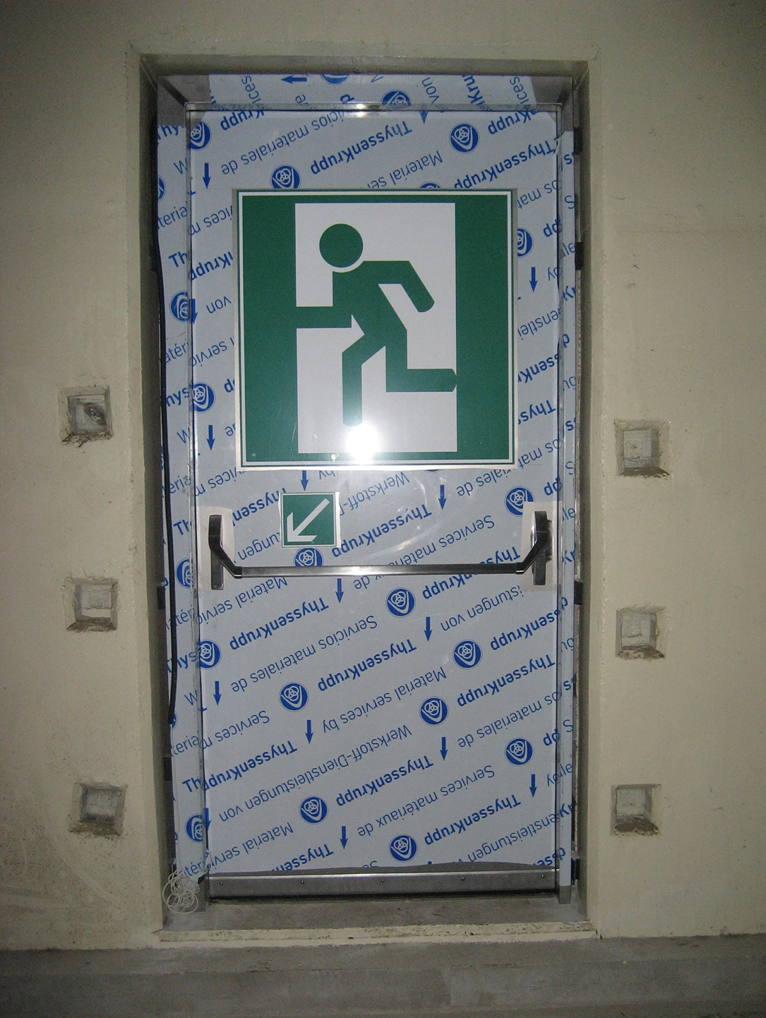 Edelstahl-Fluchttür von BUCHELE mit Schutzfolie und Notausgang-Piktogramm in einer Betonwand