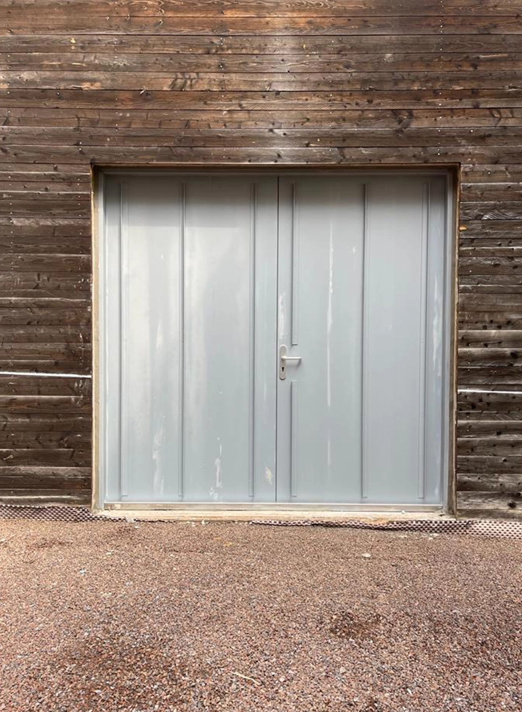 Grey double-leaf steel gate by BUCHELE in a timber facade