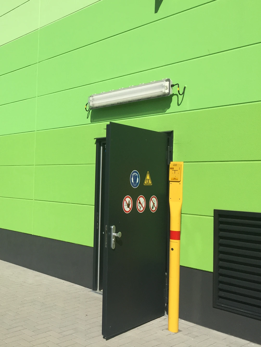 Dark green steel door with warning signs in a green facade of a transformer station