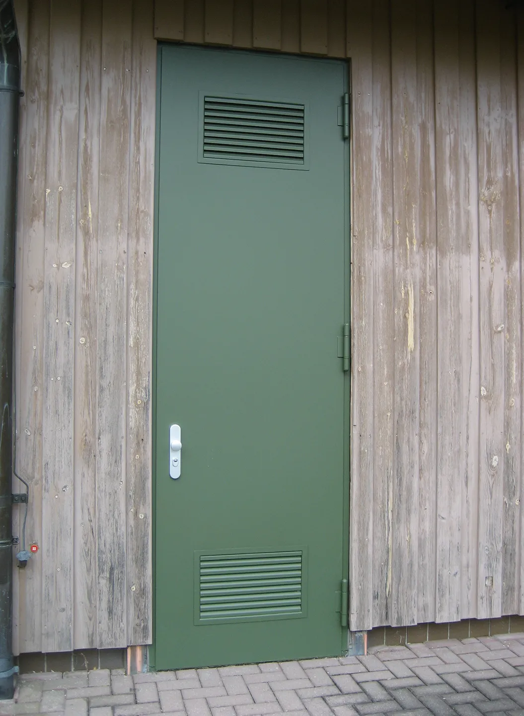 Green transformer station door with ventilation grilles in a timber facade