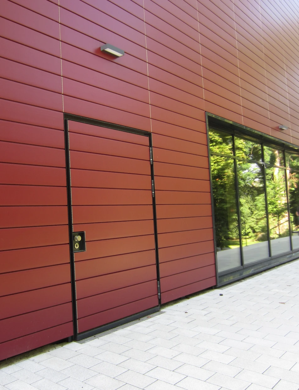 Flächenbündige BUCHELE DELUXE Tür in einer roten Metallfassade neben Glasfront