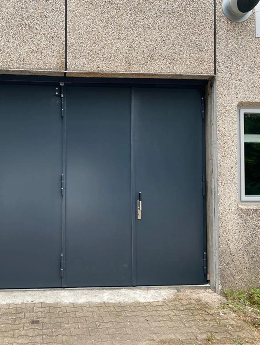 Anthracite folding gate by BUCHELE in a concrete wall