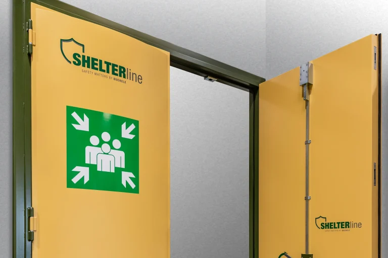 SHELTER LINE Schutzraumtür von BUCHELE in Gelb, geöffnet, mit grünem Sammelplatz-Symbol und sichtbarer Mehrpunktverriegelung